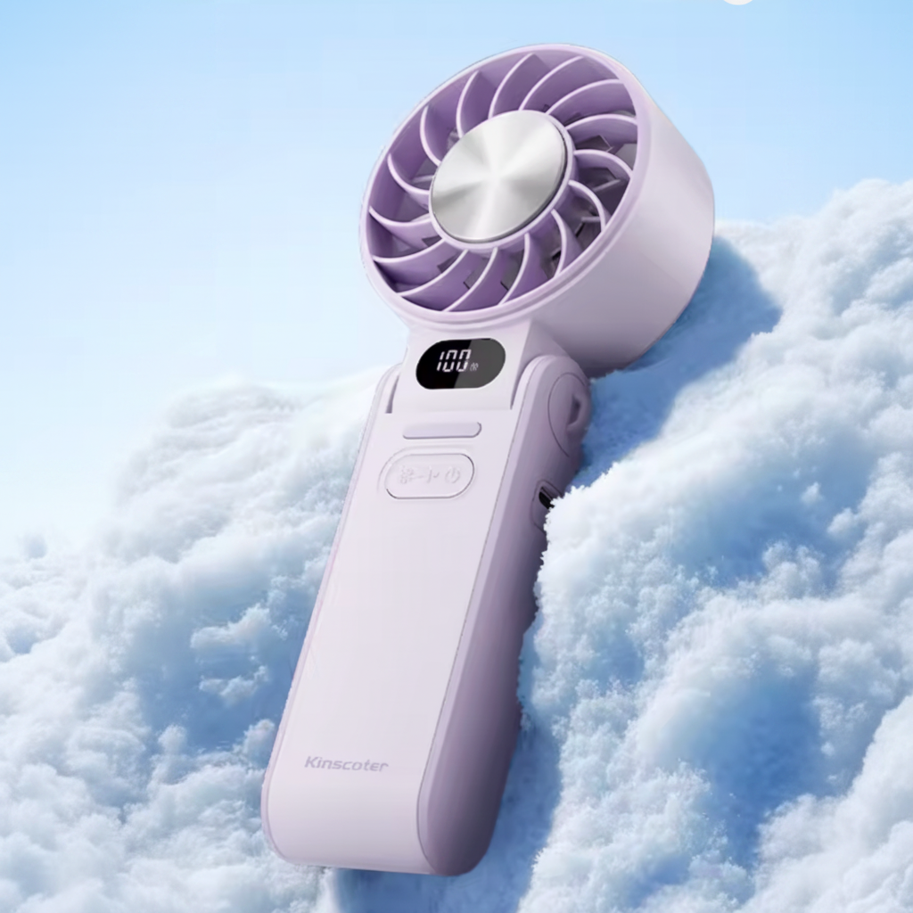 A handheld portable fan in a light lavender purple color, resting on a bed of white snow against a light blue sky background. The fan has a digital display showing '100%' and the brand name 'Kingscofe' printed near the bottom.
