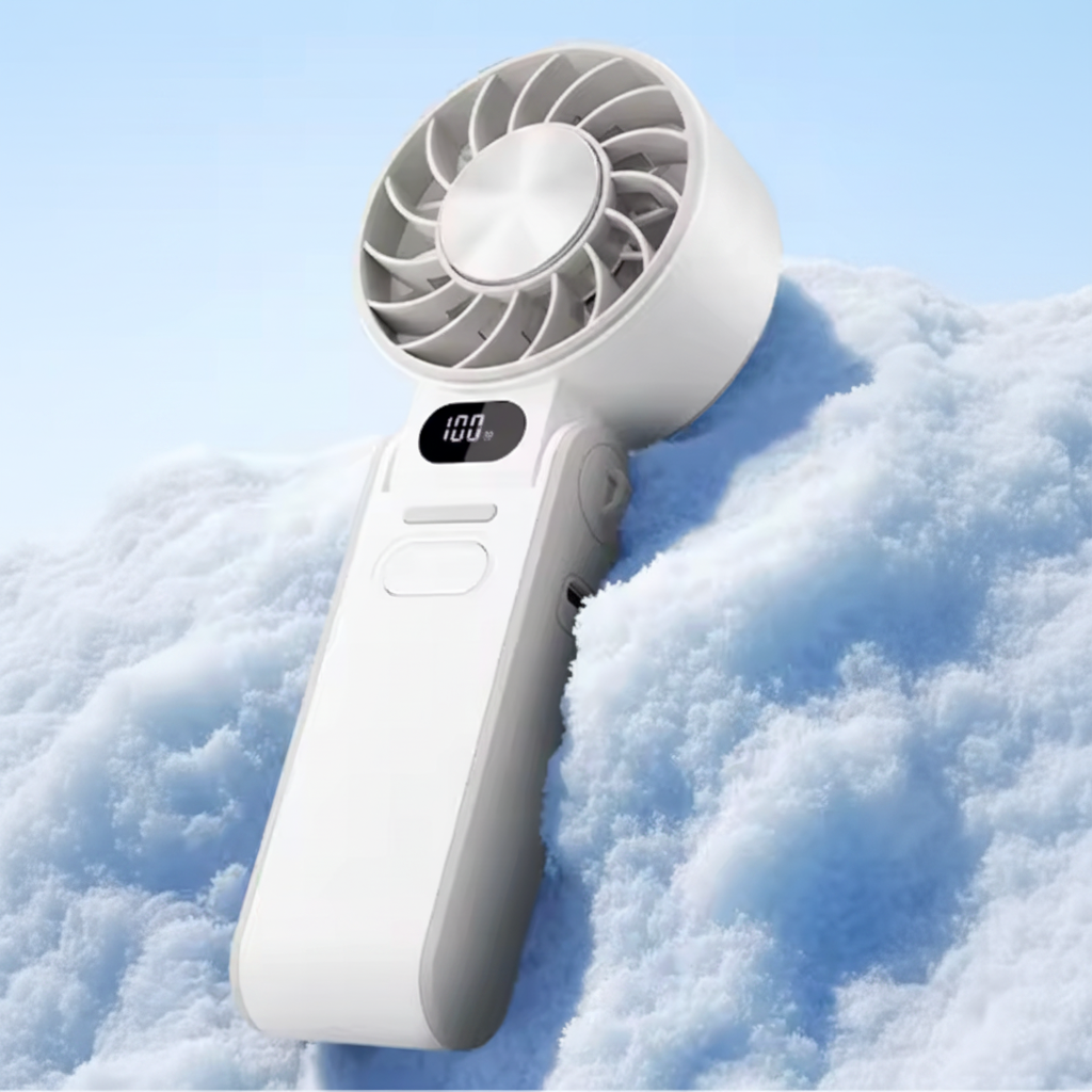 A white Kinscoter handheld portable fan with a digital display, shown resting in snow against a light blue sky background.
