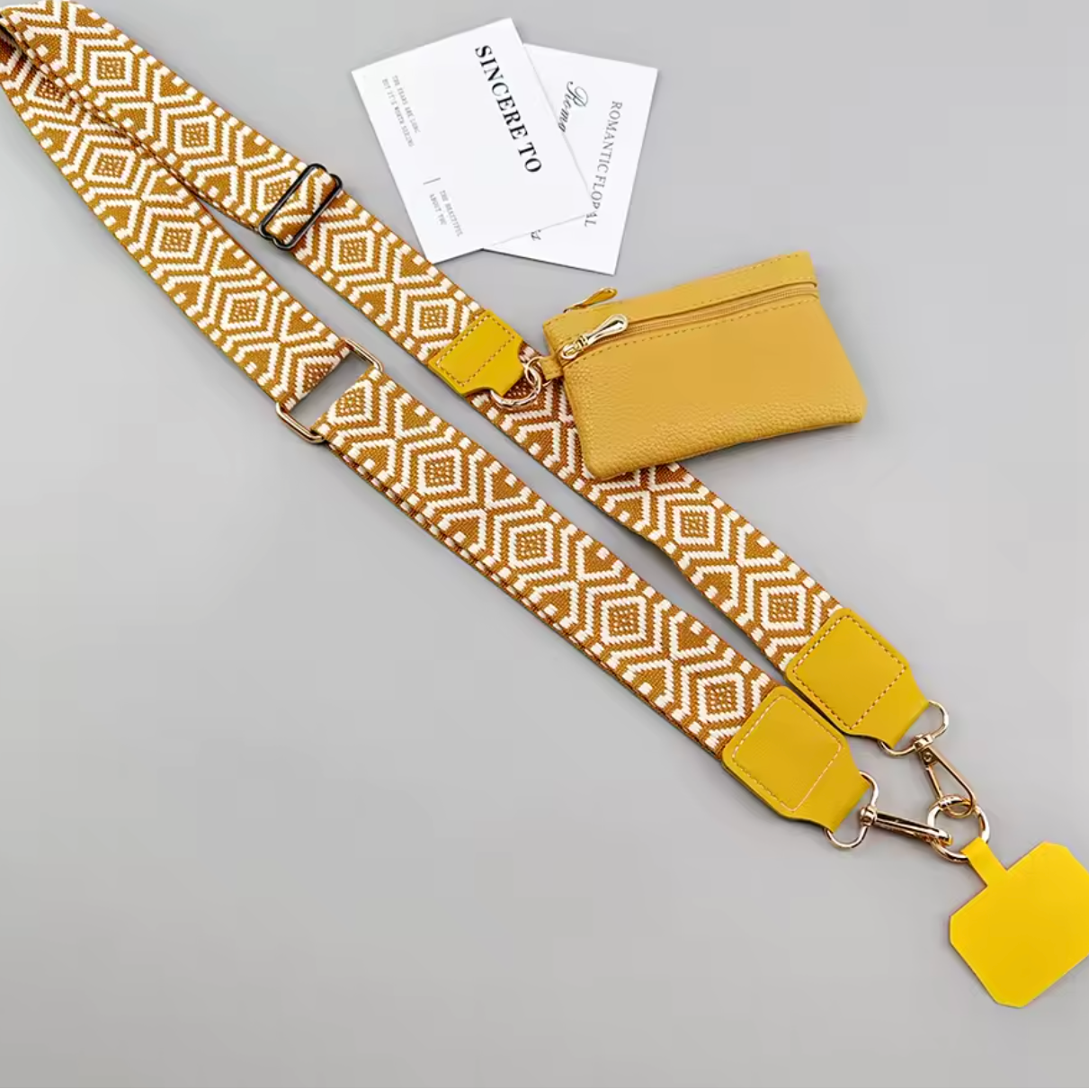 A yellow and white geometric patterned shoulder strap set with a matching zippered pouch, displayed on a light gray background with two brand cards.