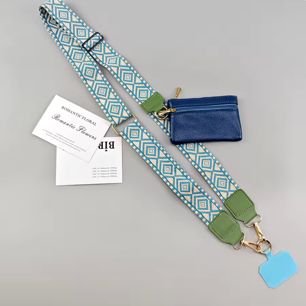 A shoulder strap bag set with a blue and white geometric patterned strap, olive green leather accents, a small blue zippered pouch, and printed cards on a light gray background.