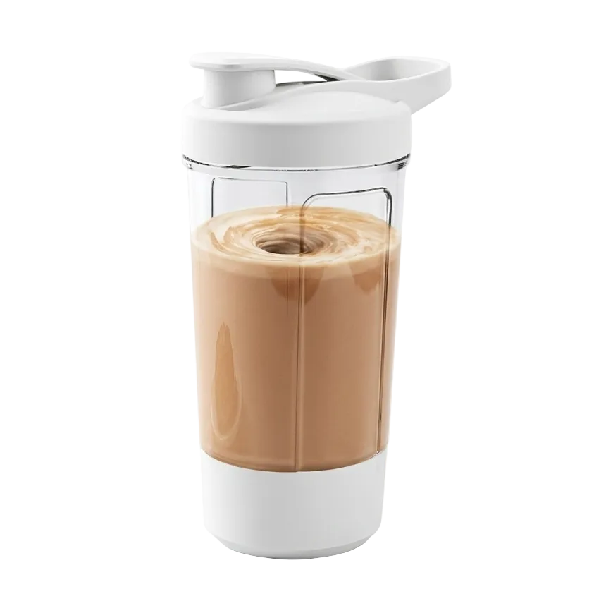 A clear personal blender cup with a white lid and base, filled with a light brown iced coffee drink, shown on a white background with a pastry partially visible on the left.