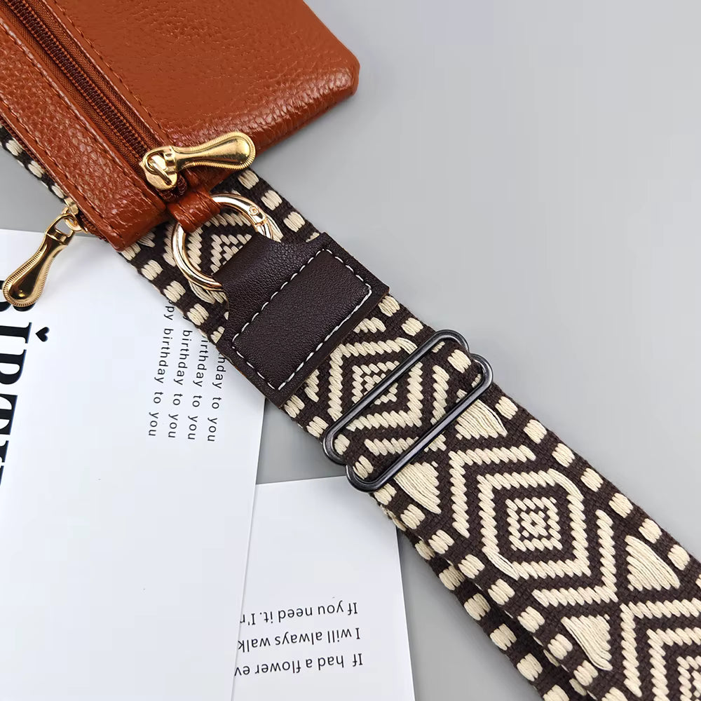 A close-up of a brown leather zip pouch attached to a wide woven shoulder strap with a cream and brown geometric diamond pattern, shown on a light gray background with printed paper props.